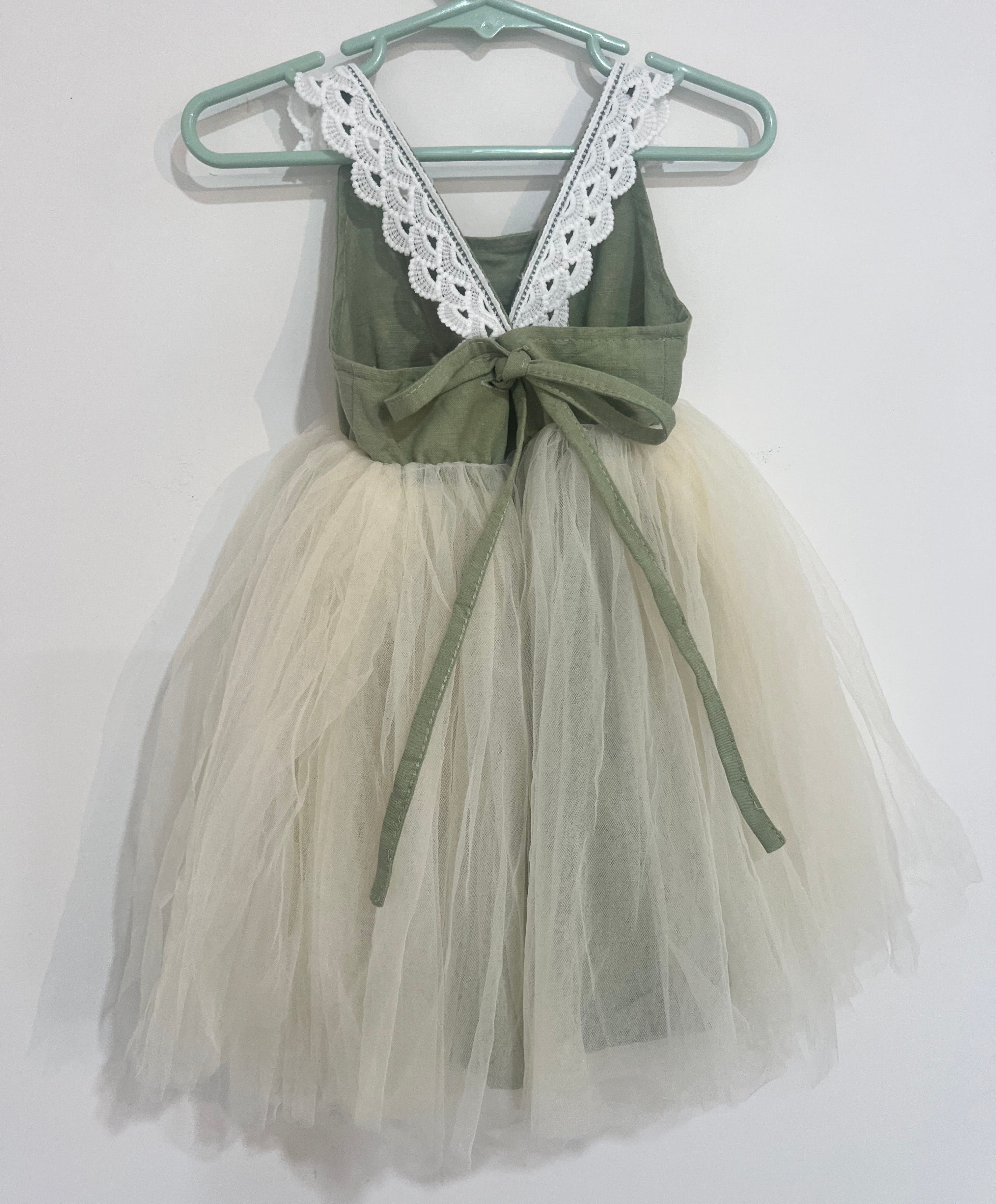 Green dress with a white tulle skirt on a hanger against a white background